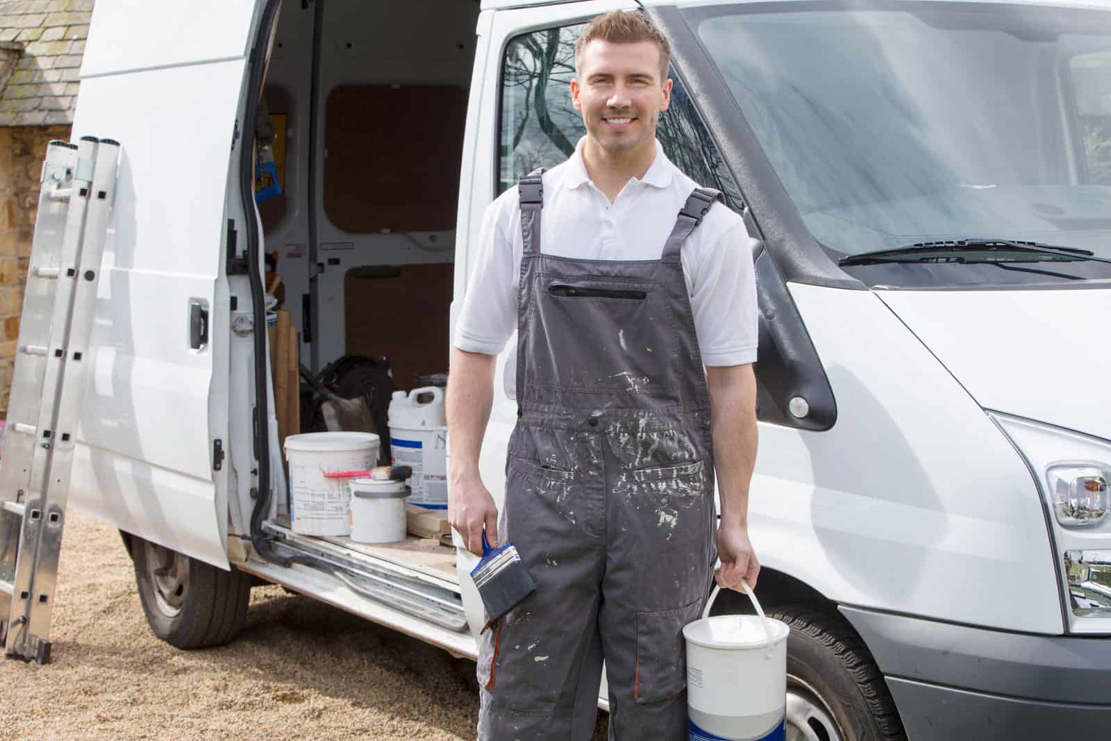 Painting Professional With Service Van Painter in gray work apron standing in front of white service van with paint supplies visible inside