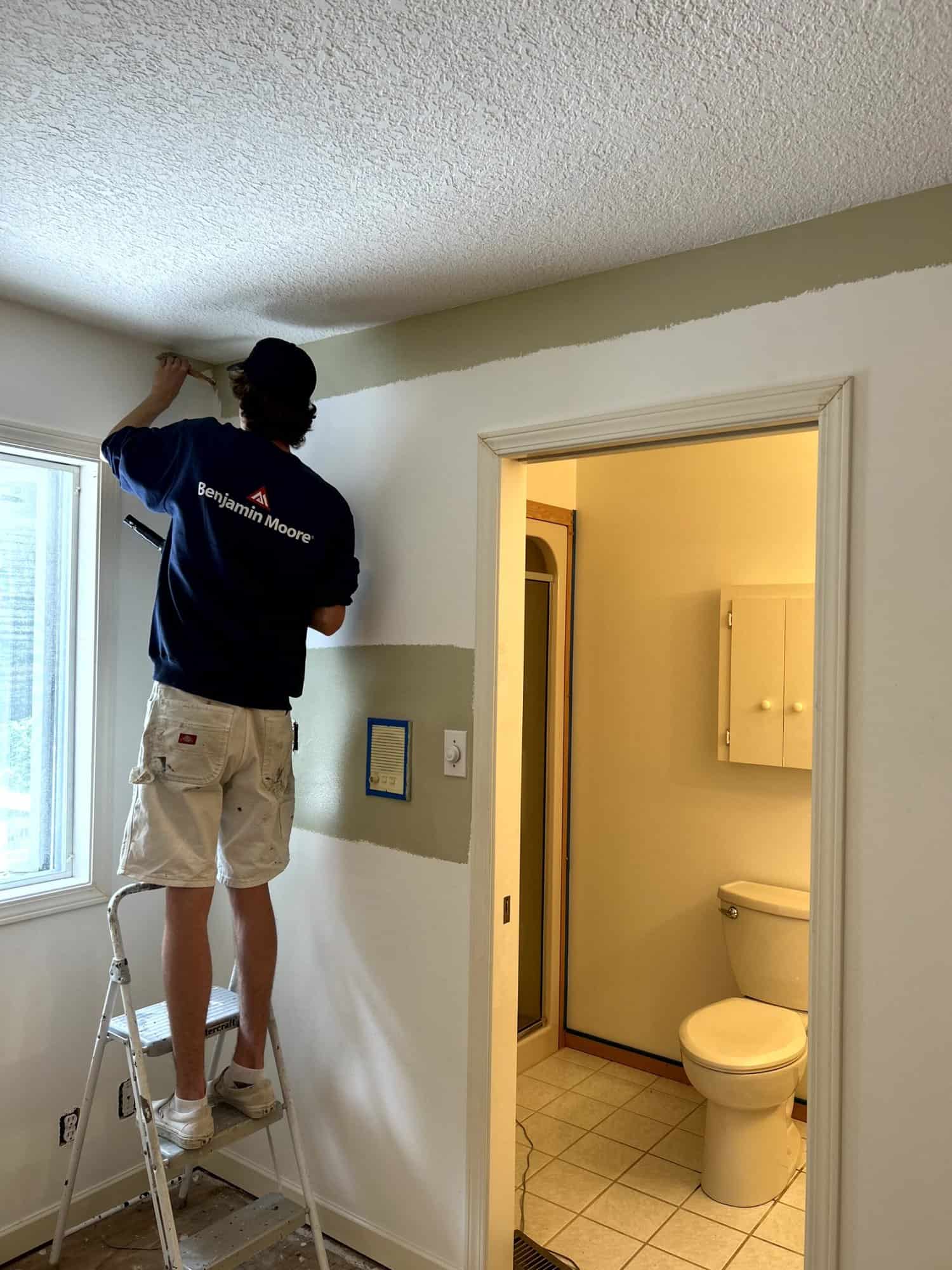 ways to protect furniture -a man on a ladder painting white on the wall