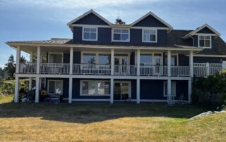 Navy blue-painted residential home with white trim, white railings, dormer windows, and covered deck structure in