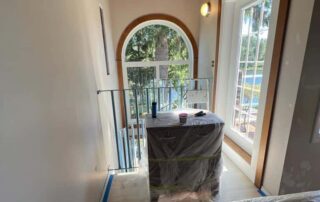 Cream-painted residential interior hallway with arched doorway, wood trim, and protective plastic on furniture