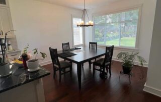 Cream-painted residential dining room with black dining table, dark wood flooring, and large windows
