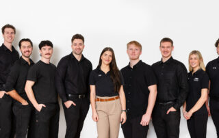 Nine professional painters and contractors in matching black uniforms and branded shirts standing against white background how to choose a painter Nanaimo