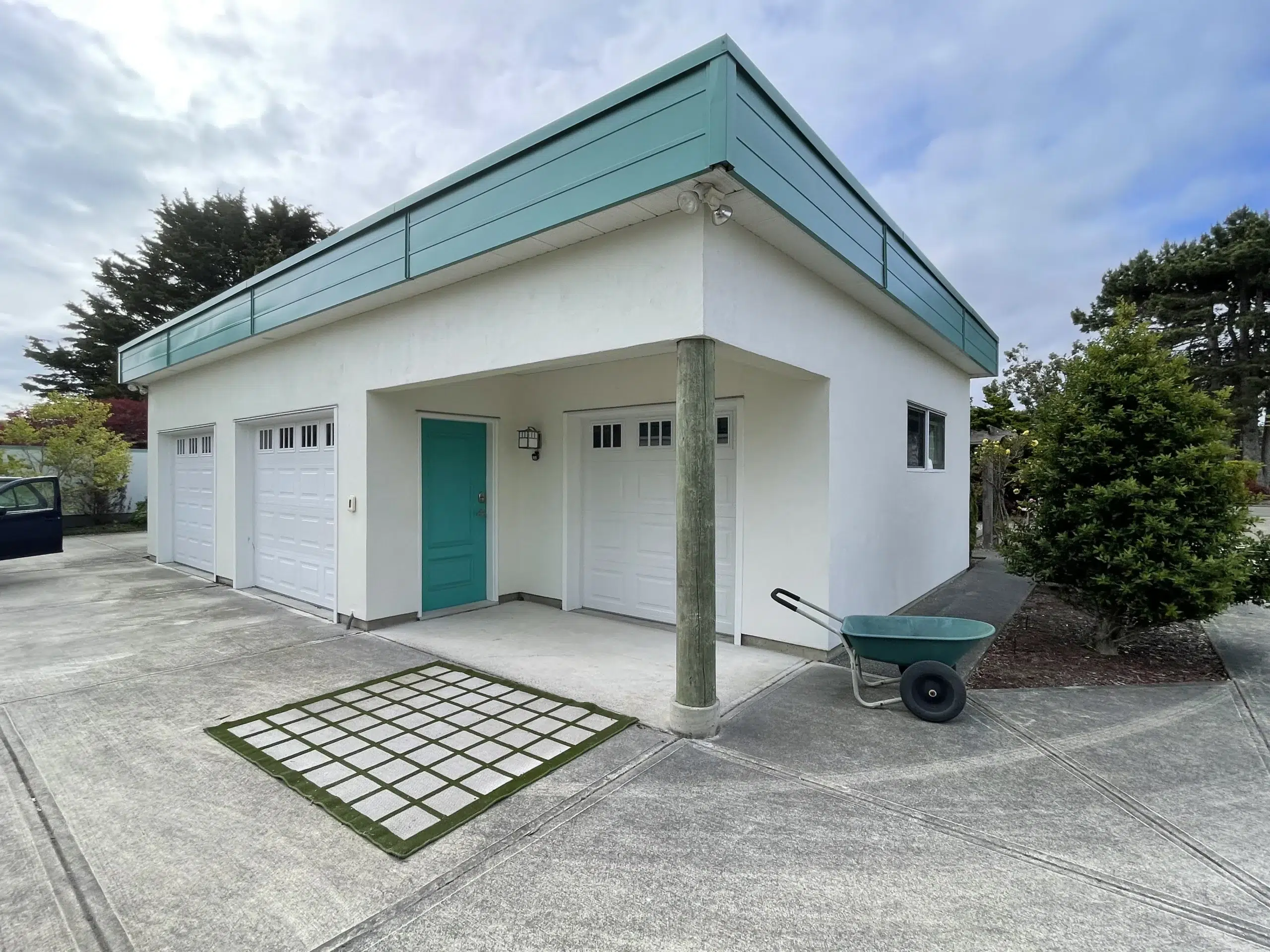 Modern White Residential Home Teal Trim Modern white-painted residential home with teal metal roofline, white garage doors, teal entry door, and concrete driveway