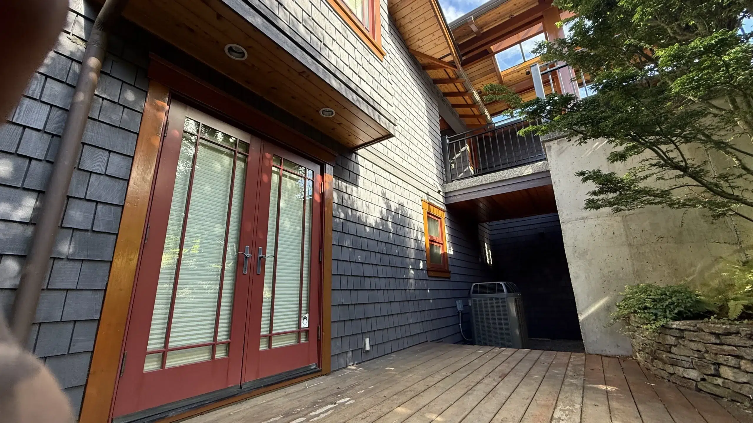 Modern Home Exterior with Dark Shingle Siding Dark blue-gray shingle siding residential home with red-stained entry door, warm wood trim, and wooden deck in Parksville, BC