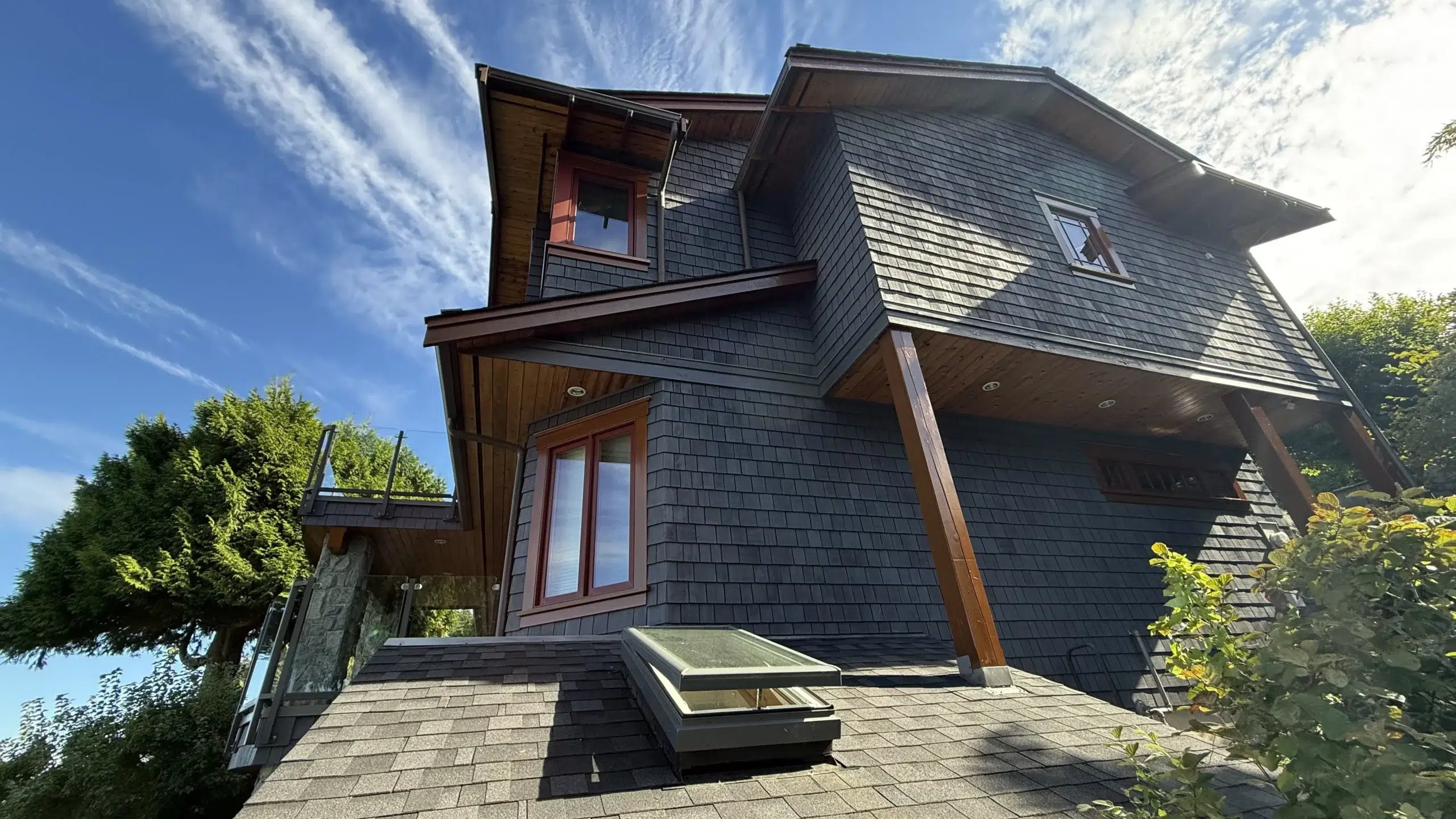 Dark Gray Shingle Siding Home Dark gray shingle siding residential home with warm wood trim, red-stained entry door, and stone patio in Parksville, BC