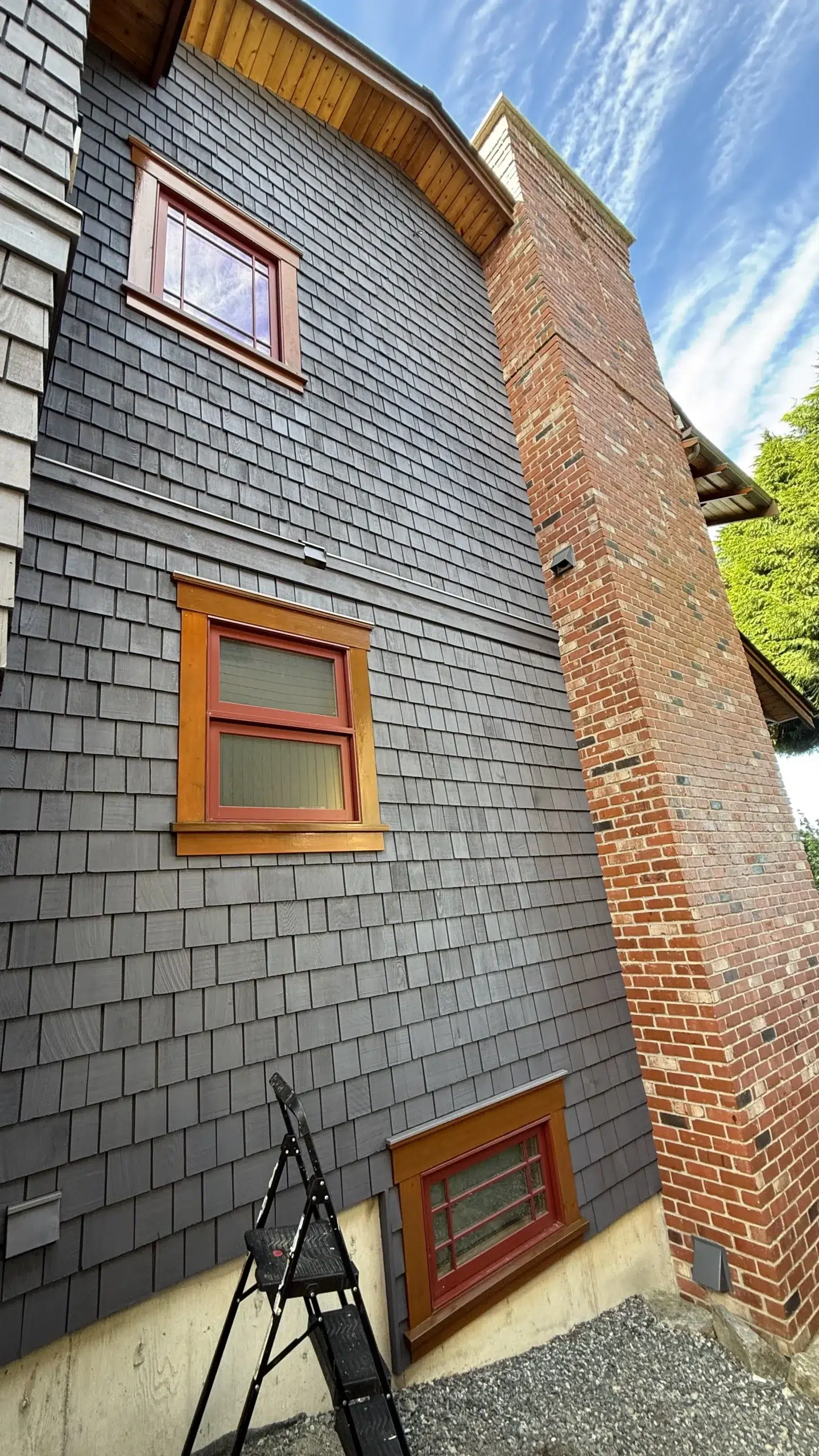 Charcoal Shingle Siding With Warm Wood Trim Charcoal-painted shingle siding residential exterior with warm wood-trim windows, red-stained frames, and brick chimney in